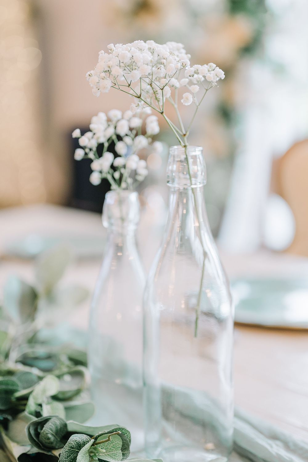 Delicate white baby's breath flowers arranged in clear glass bottles on a table setting.