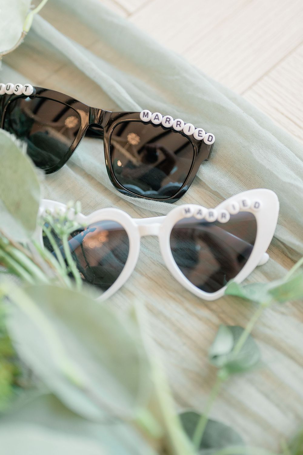 White rhinestone-embellished sunglasses displayed on a light wooden surface with soft focus background.