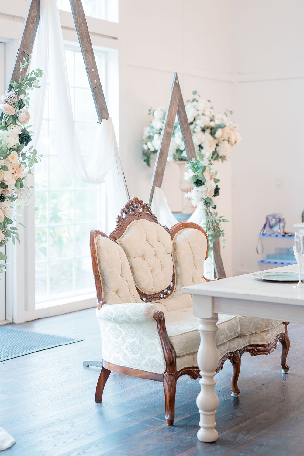Elegant vintage-style cream chaise lounge with ornate wooden frame decorated with floral garlands and delicate lighting.
