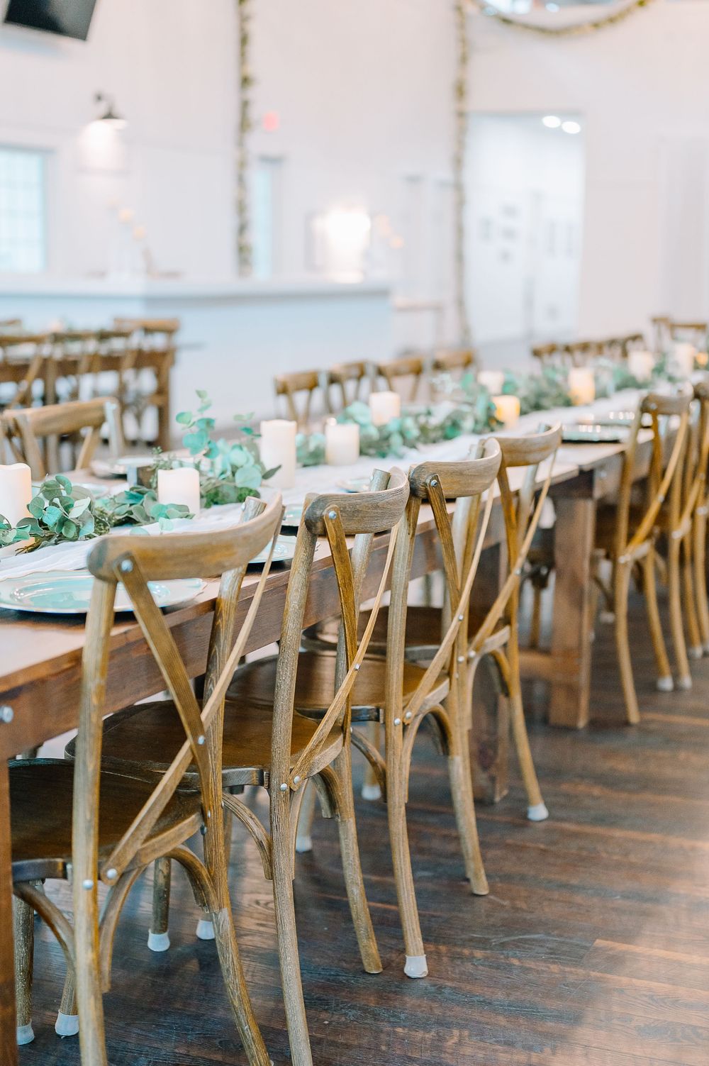 Long wooden tables with elegant place settings and centerpieces set up for a rustic wedding reception.