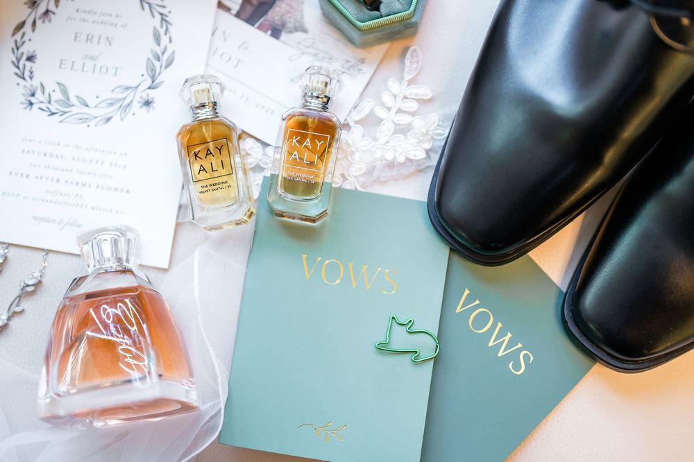 Elegant wedding details including vintage perfume bottles, vows booklet in mint green, and black dress shoes on flat lay.