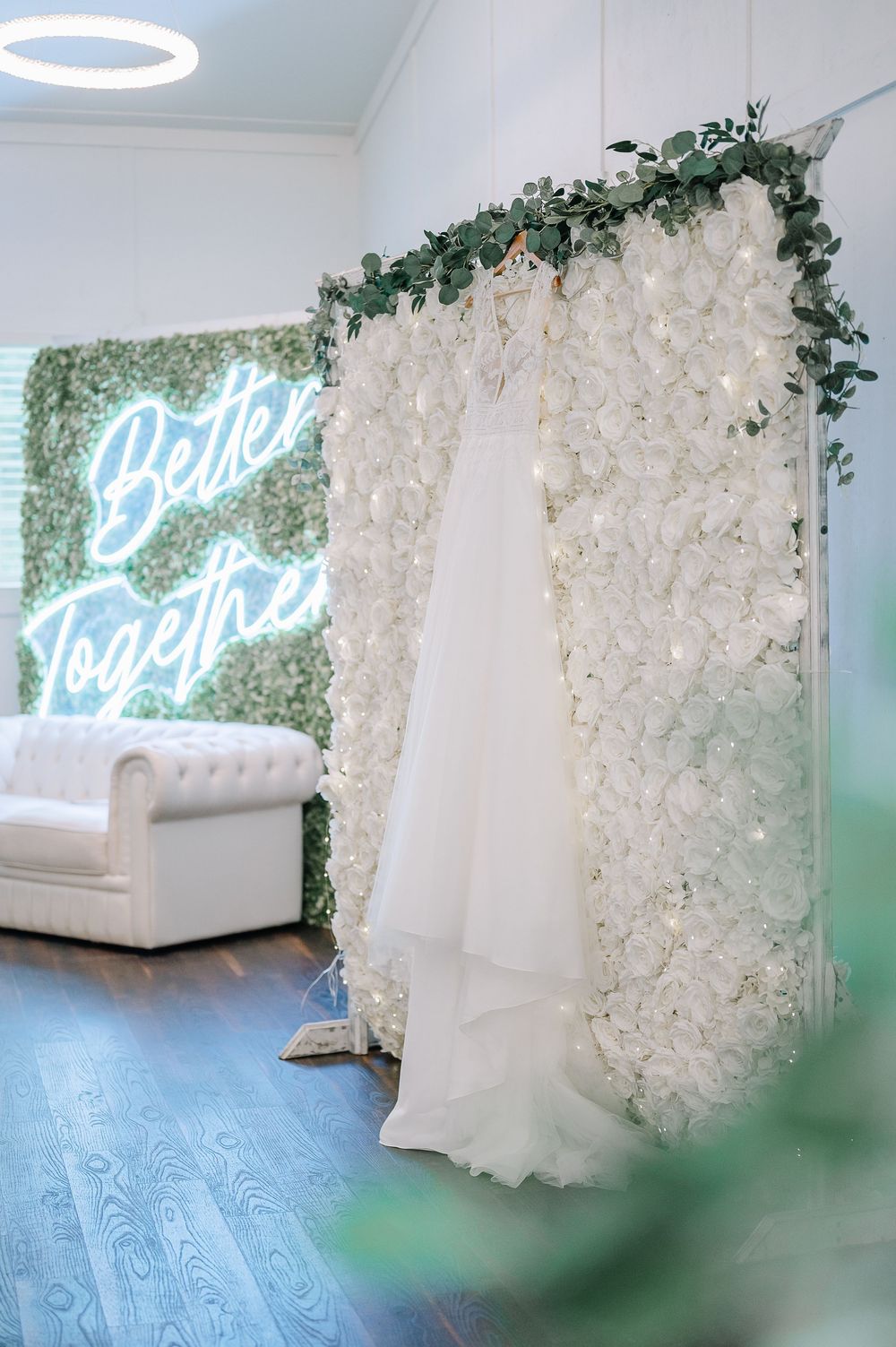 Elegant white floral wall backdrop with neon sign and seating arrangement for wedding reception.