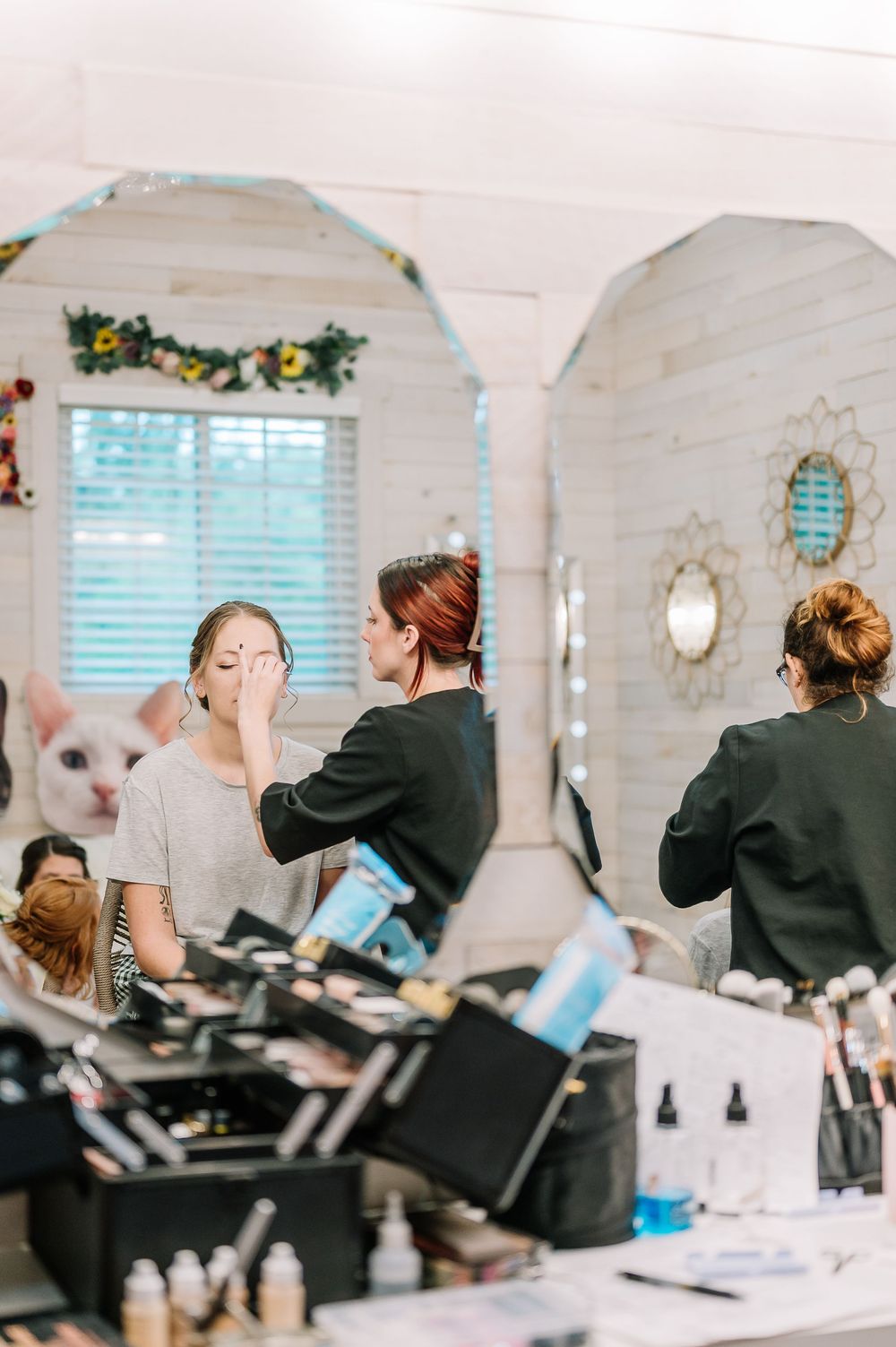 Several people in black attire stand at beauty stations in a bright white salon space.