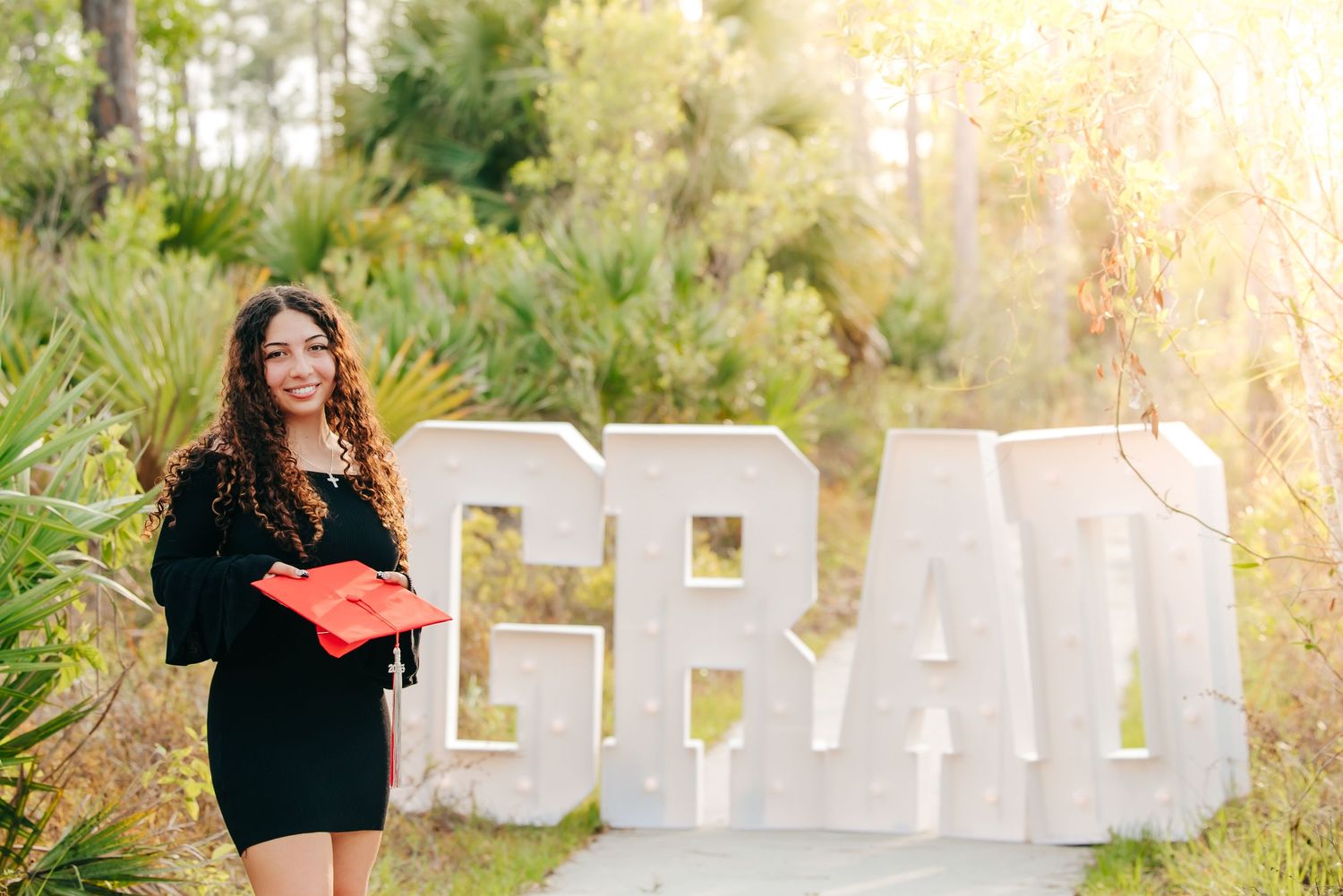 Golden sunlight filters through trees in an outdoor senior photo session as figure stands against natural backdrop.
