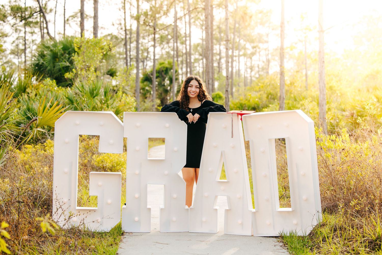 Large decorative white letters spelling 'GRAD' create photo opportunities in a sunlit outdoor setting with pine trees.