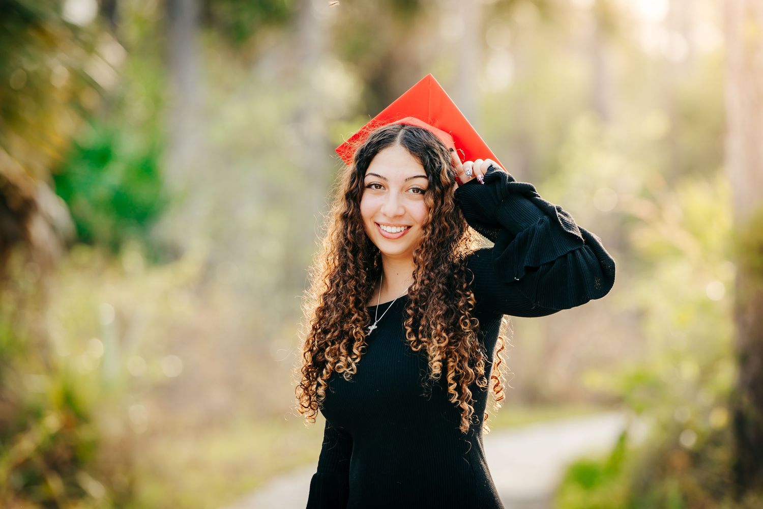 Person in black outfit poses in a natural outdoor setting with soft golden sunlight filtering through trees.
