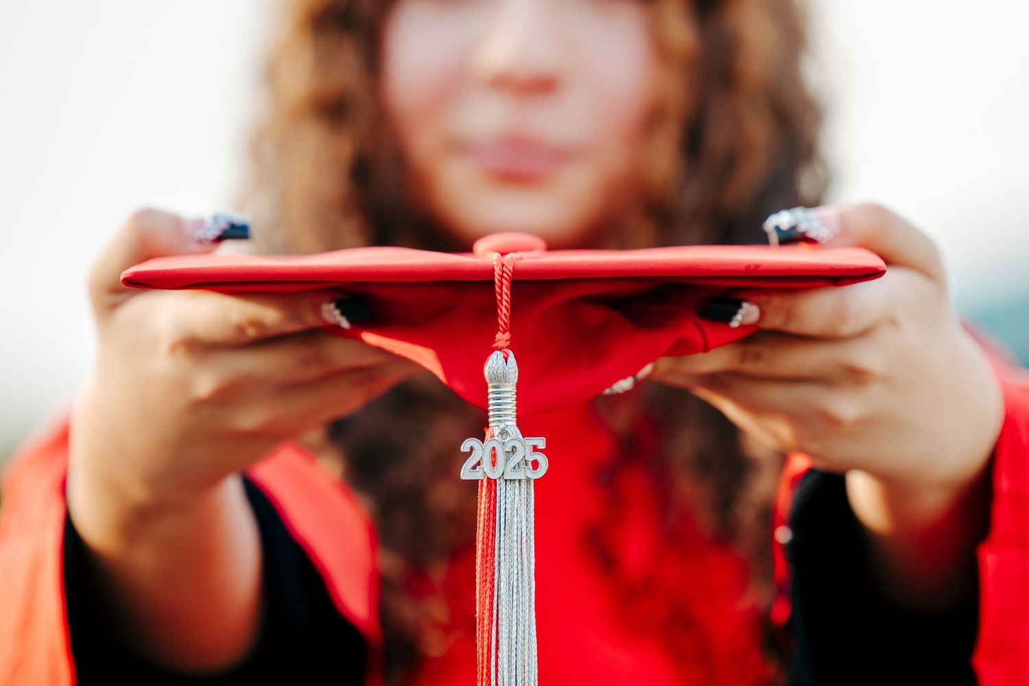 Someone holding a red 2025 graduation tassel with blurred background.