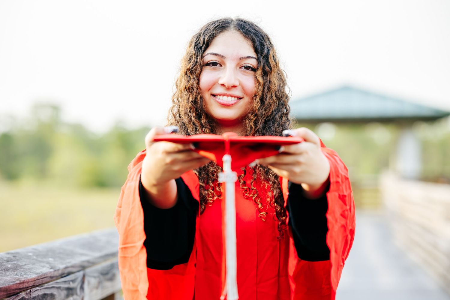 A person walks along a train track while holding a bright red umbrella against an overcast sky.