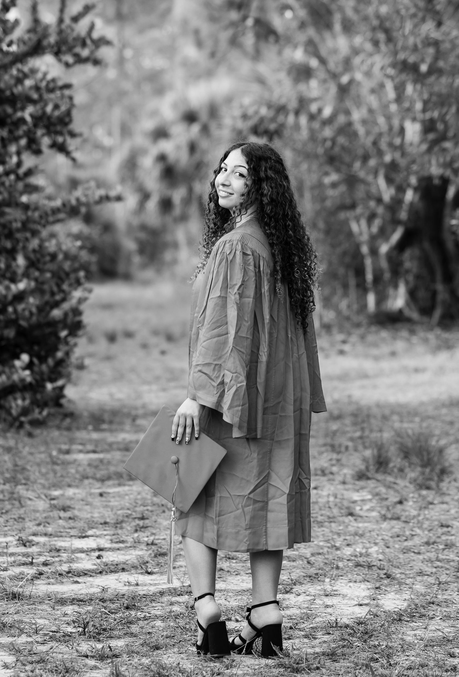 Black and white portrait of a person with curly hair holding a notebook while standing on a garden pathway.
