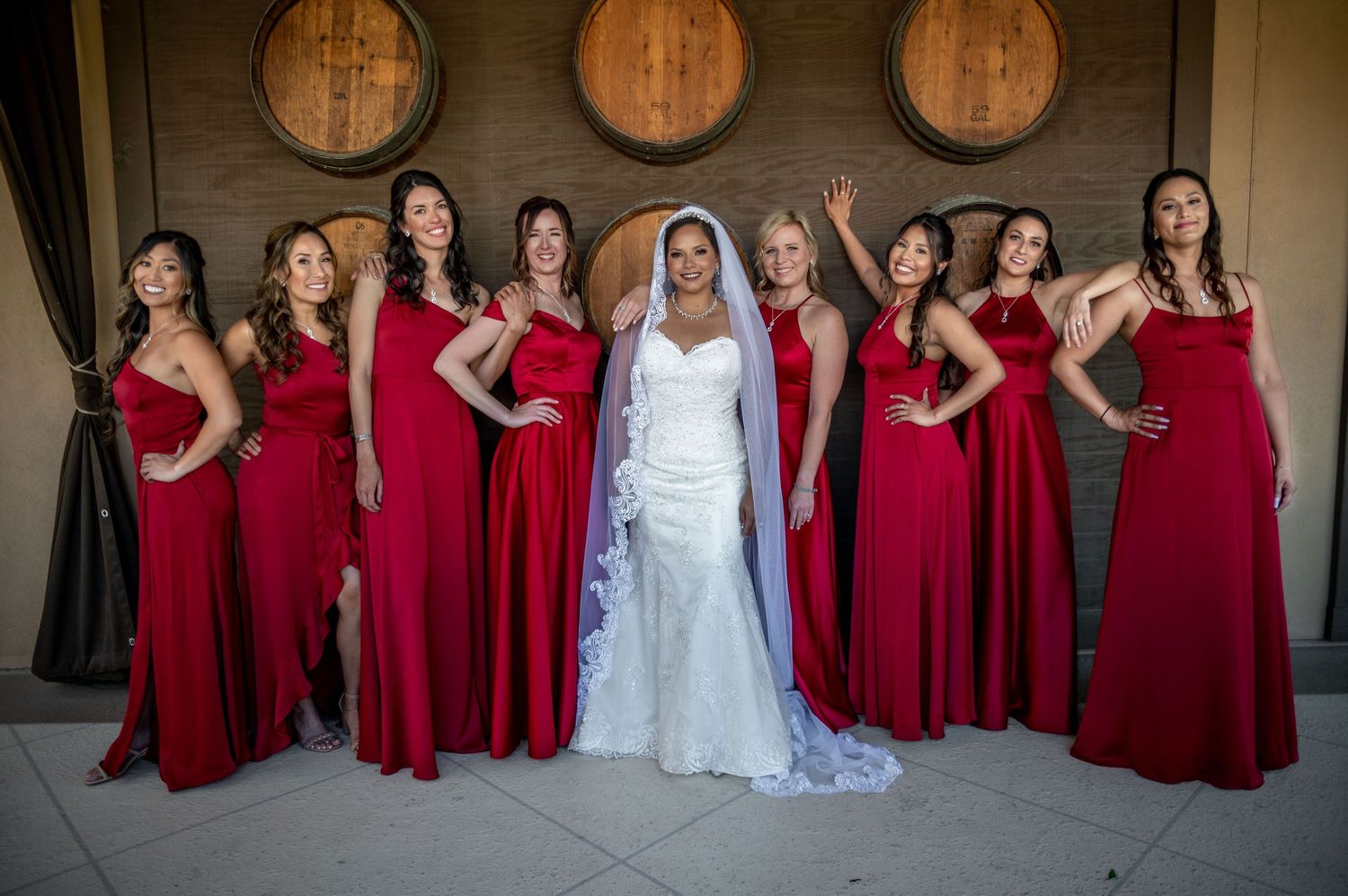 A line of bridesmaids in burgundy dresses pose with the bride in white for a wedding photo.