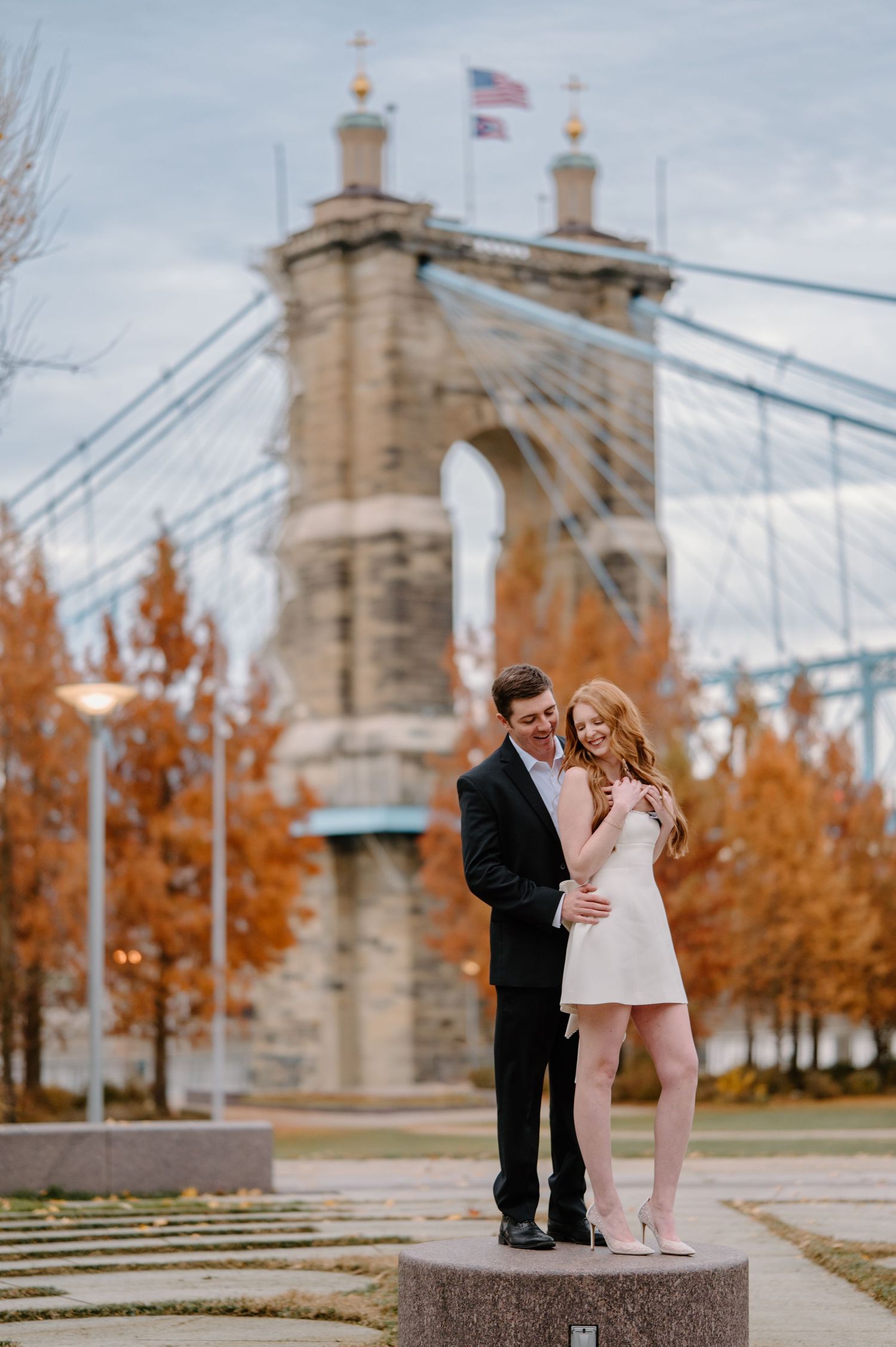 A romantic couple shares a loving embrace against the Cincinnati skyline during golden hour.