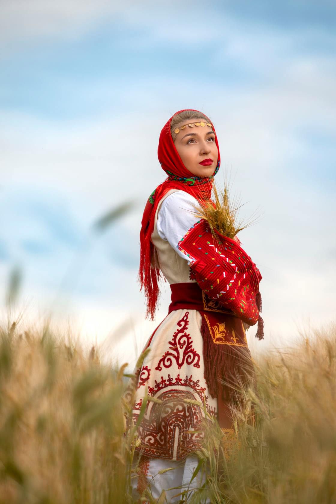Traditional folk costume in red and white photographed in wheat field at golden hour.