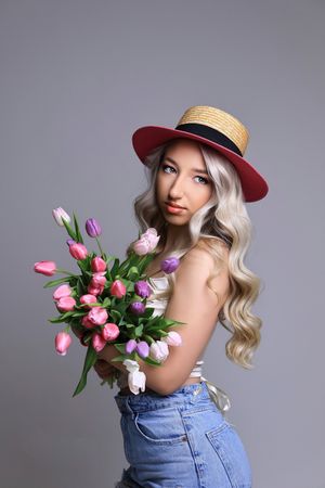 Fashion portrait series with tulip bouquet, straw hat, and denim outfit against gray backdrop.