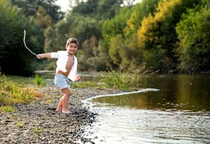Someone skips stones across a tranquil river surrounded by green trees on a sunny summer day.
