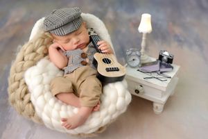 Newborn baby sleeping on white knit blanket with miniature guitar prop.