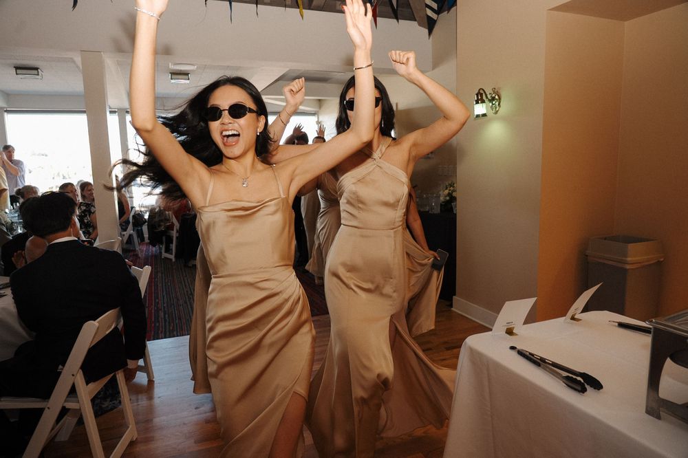 Bridesmaids in beige dresses dancing and celebrating at an indoor wedding reception.