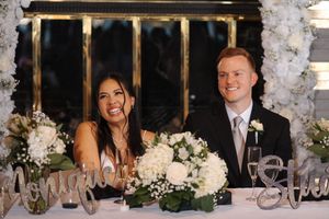 Wedding reception guests seated at a long table decorated with white floral centerpieces and candelabras.