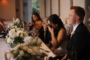 Wedding guests seated at long dinner tables with white floral centerpieces in an elegantly lit reception venue.