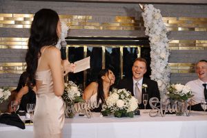People gather at a wedding reception event with table settings and decorations in an indoor venue.