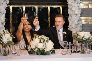 A long table at a wedding reception is decorated with floral arrangements and candles while guests celebrate and dine.