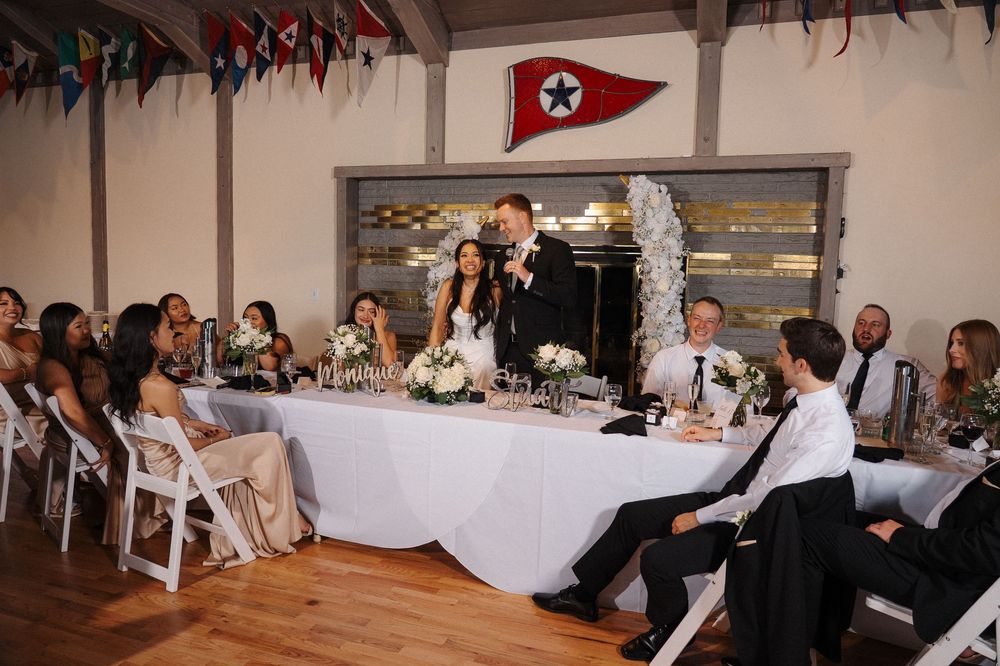 Wedding reception panorama showing guests seated at long tables in a decorated indoor venue.