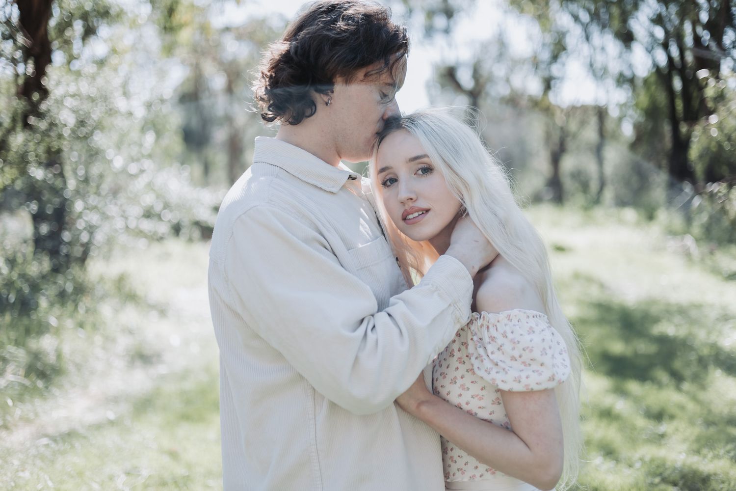 Couple during a Perth park photoshoot, man kissing his partner’s head as she looks toward the camera