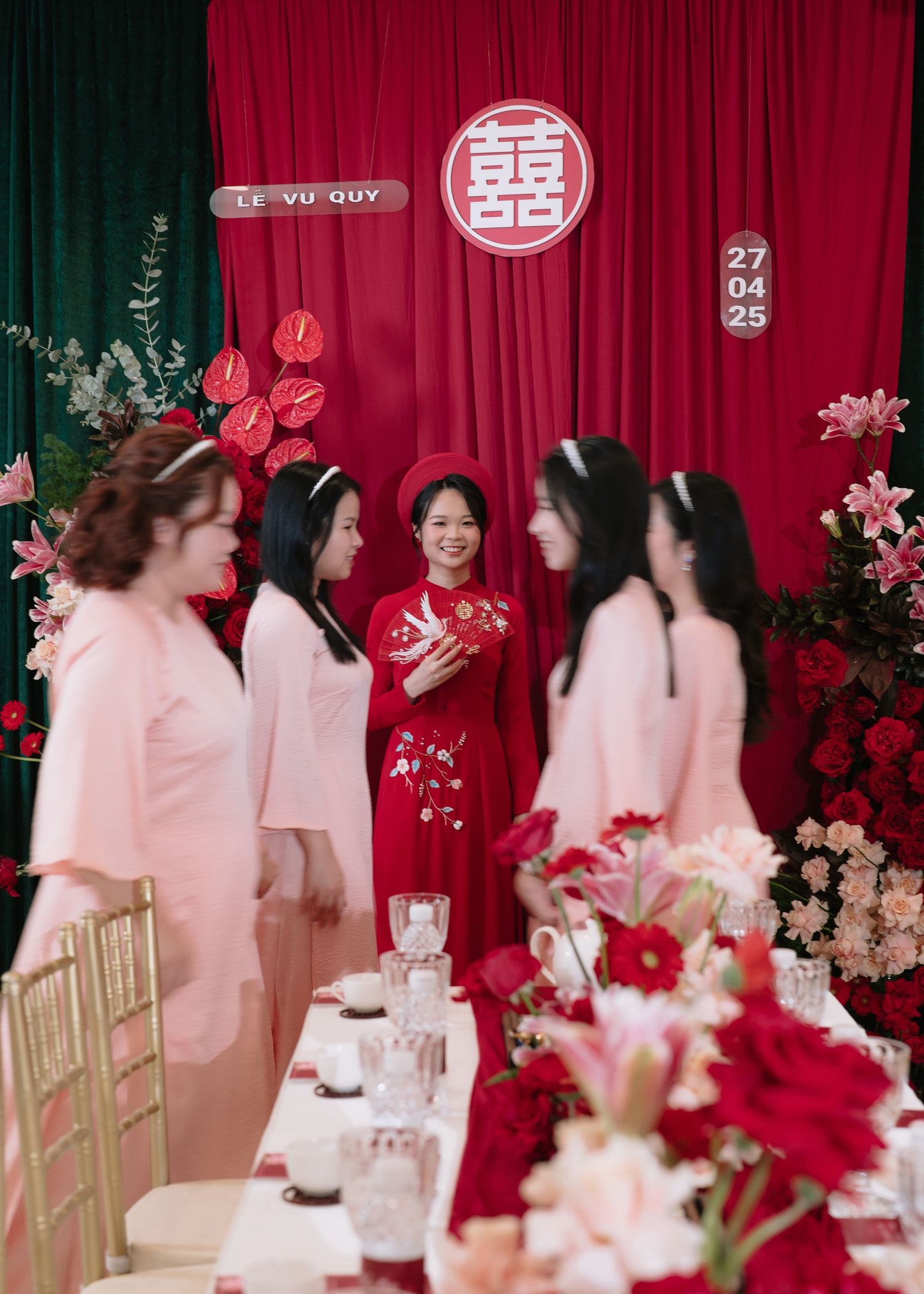 Vietnamese bride in red ao dai smiles with bridesmaids in pink at traditional Le Vu Quy ceremony.