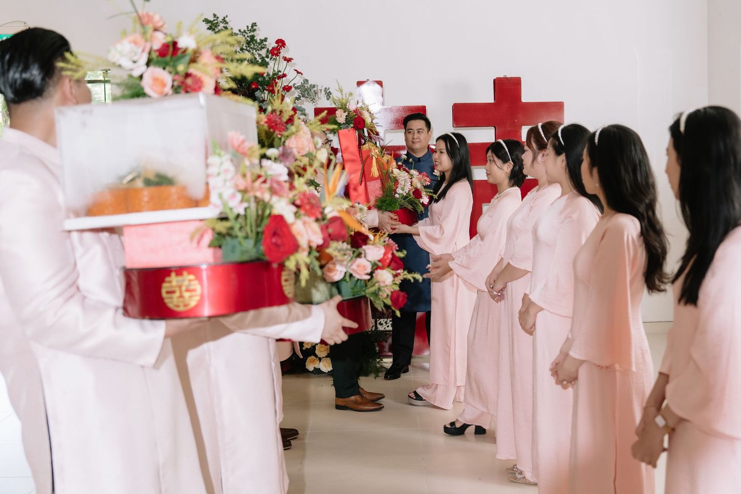 Traditional Vietnamese wedding procession with guests in pink ao dai carrying lacquered gift boxes.