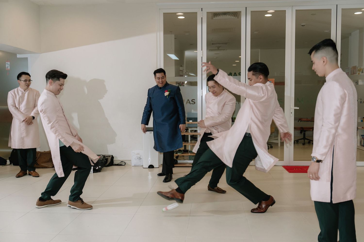 Groomsmen in pink ao dai play a lively game watched by groom at Vietnamese wedding.