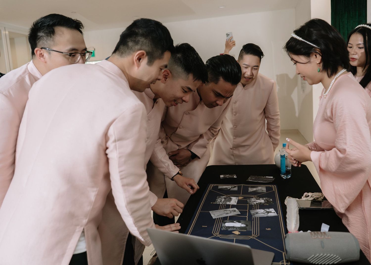 Groomsmen in pink ao dai examine wedding items on a navy blue decorated table at a Vietnamese wedding ceremony.