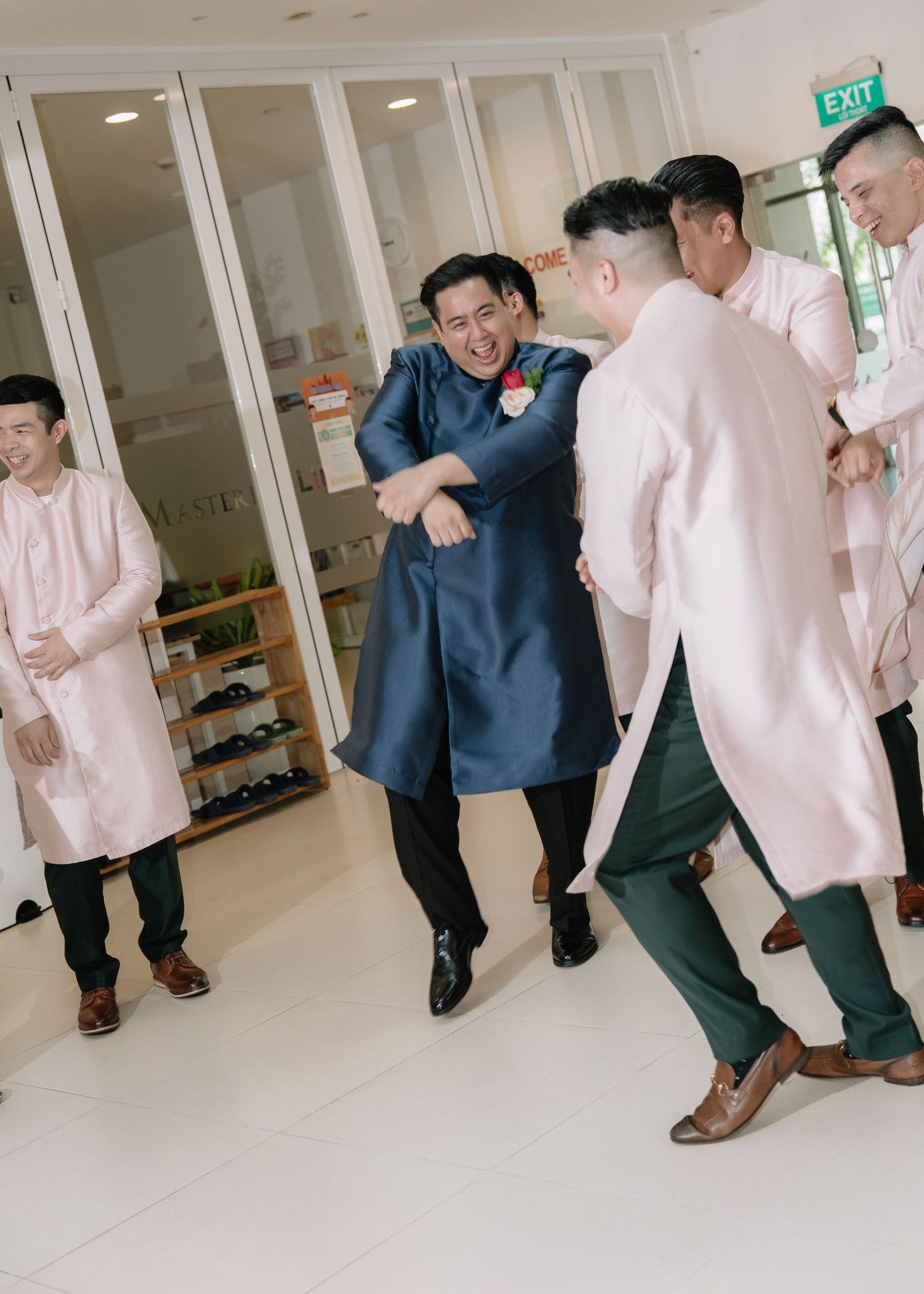 Groom in navy ao dai laughs with groomsmen in pink ao dai during a fun Vietnamese wedding door game.