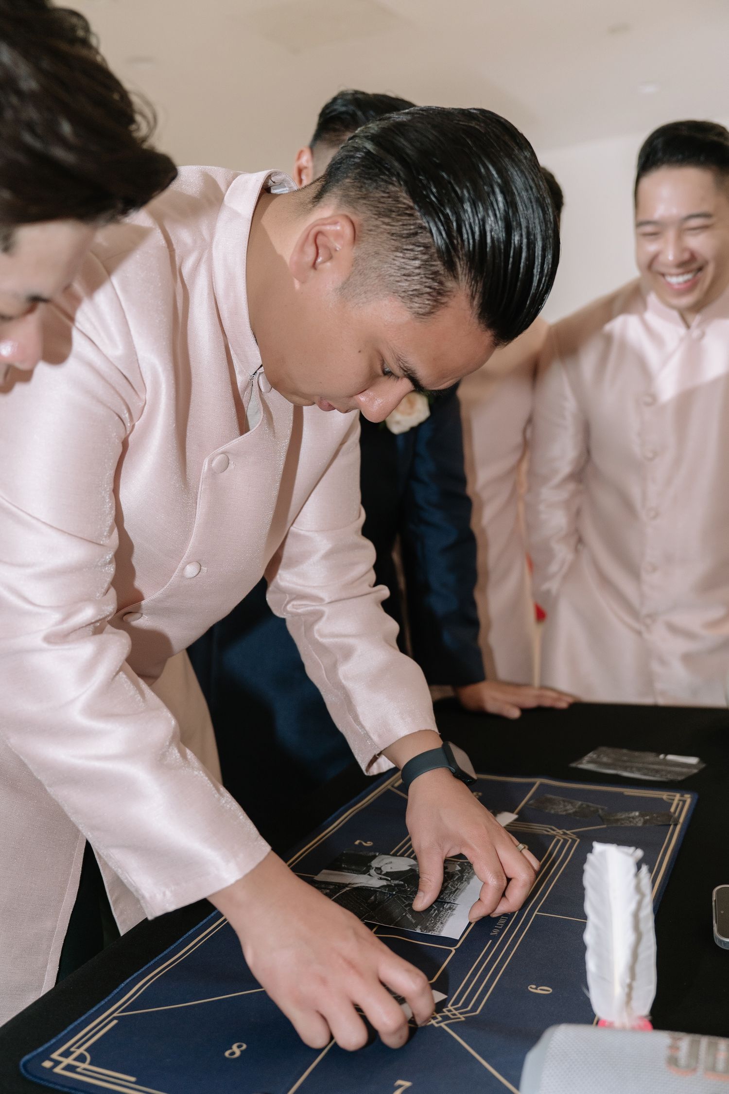 Young man in pink ao dai concentrates while completing a wedding game challenge at a Vietnamese celebration.