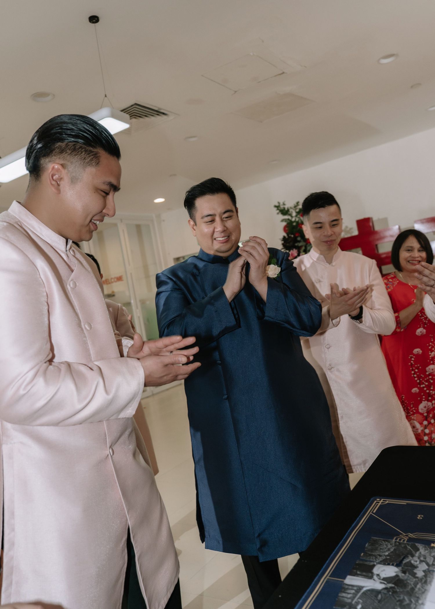 Groom in navy ao dai bows respectfully to groomsmen in pink during a traditional Vietnamese wedding ritual.