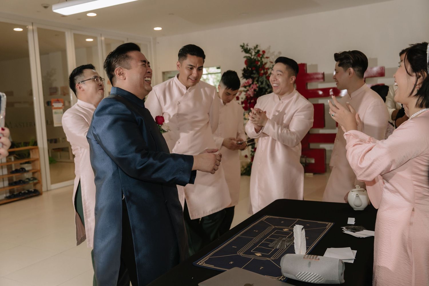 Groom in navy ao dai greets groomsmen in pink ao dai with joyful celebration at a Vietnamese wedding.