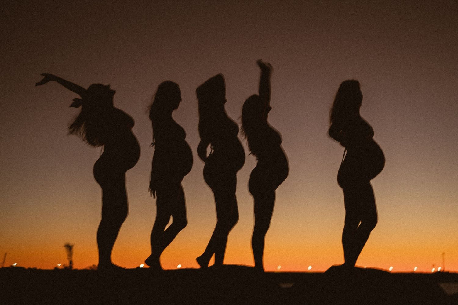 Silhouettes of people posing playfully against dramatic sunset sky.