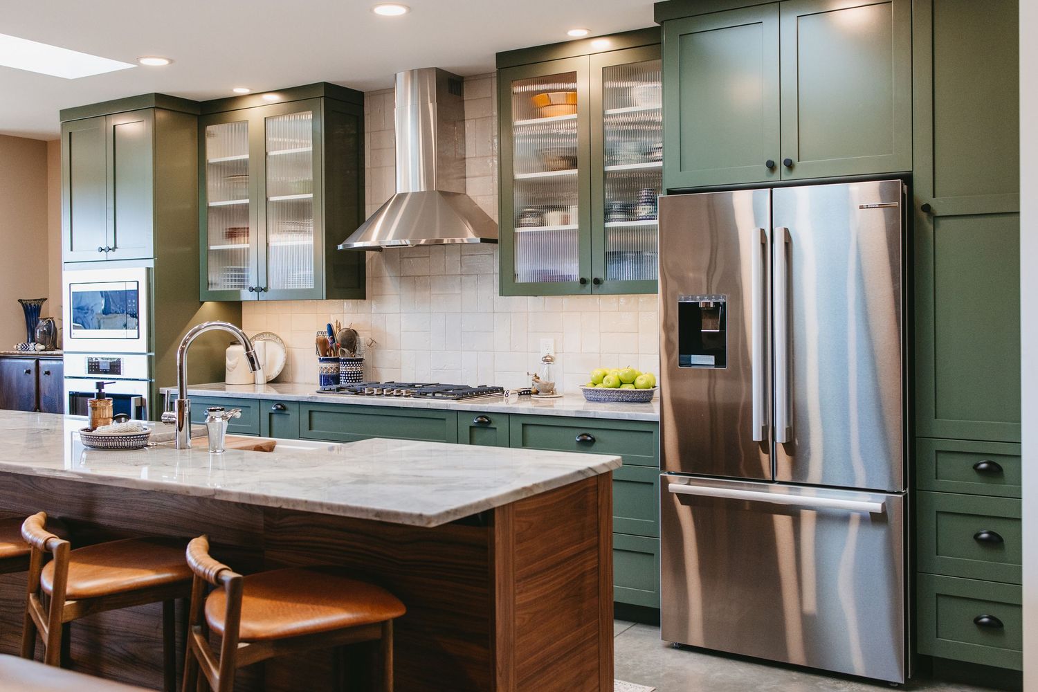 a luxurious kitchen with sage green cabinets, stainless steel appliances, granite countertops, and orange leather barstools