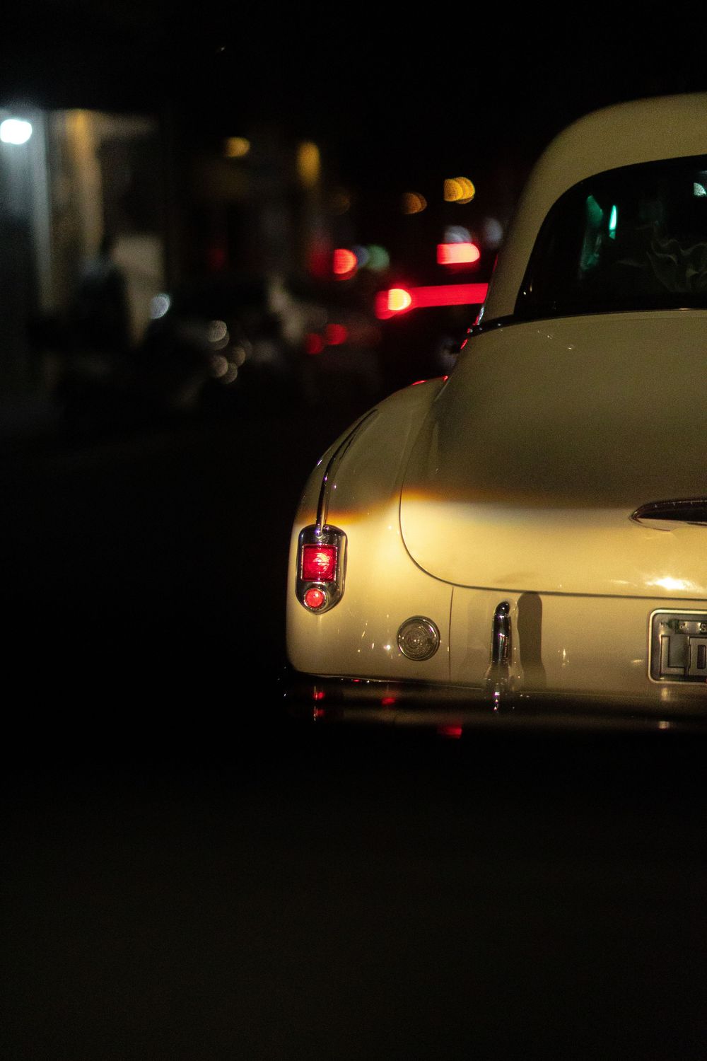 A white classic car photographed at night with red taillights glowing in the darkness, showing multiple rear angles.