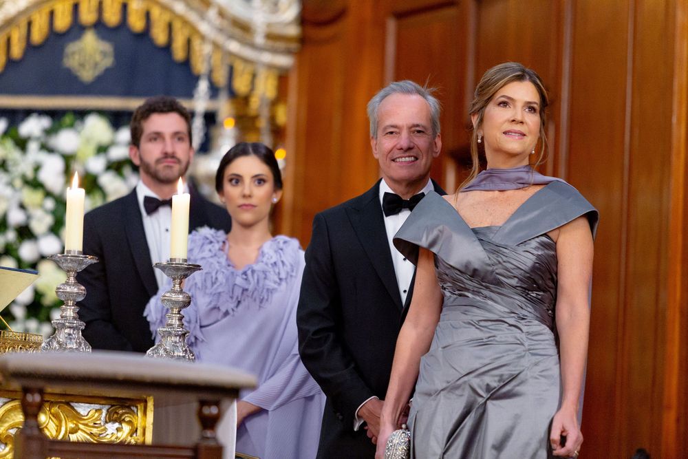 Formal event guests pose in elegant evening attire at an ornate venue decorated with golden accents.