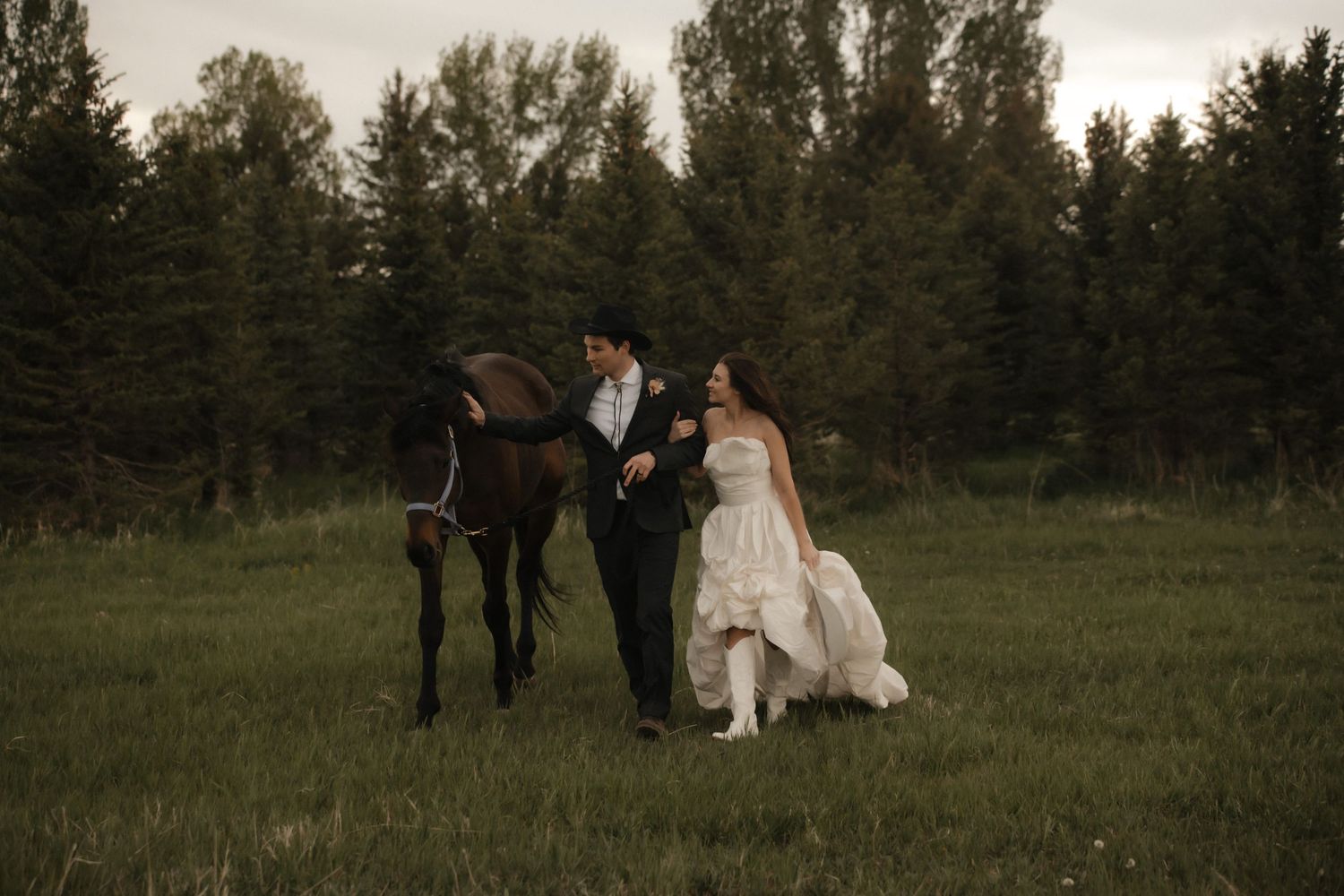 Bride and groom share intimate moment with their black horse during golden hour wedding photo session in grassy field.