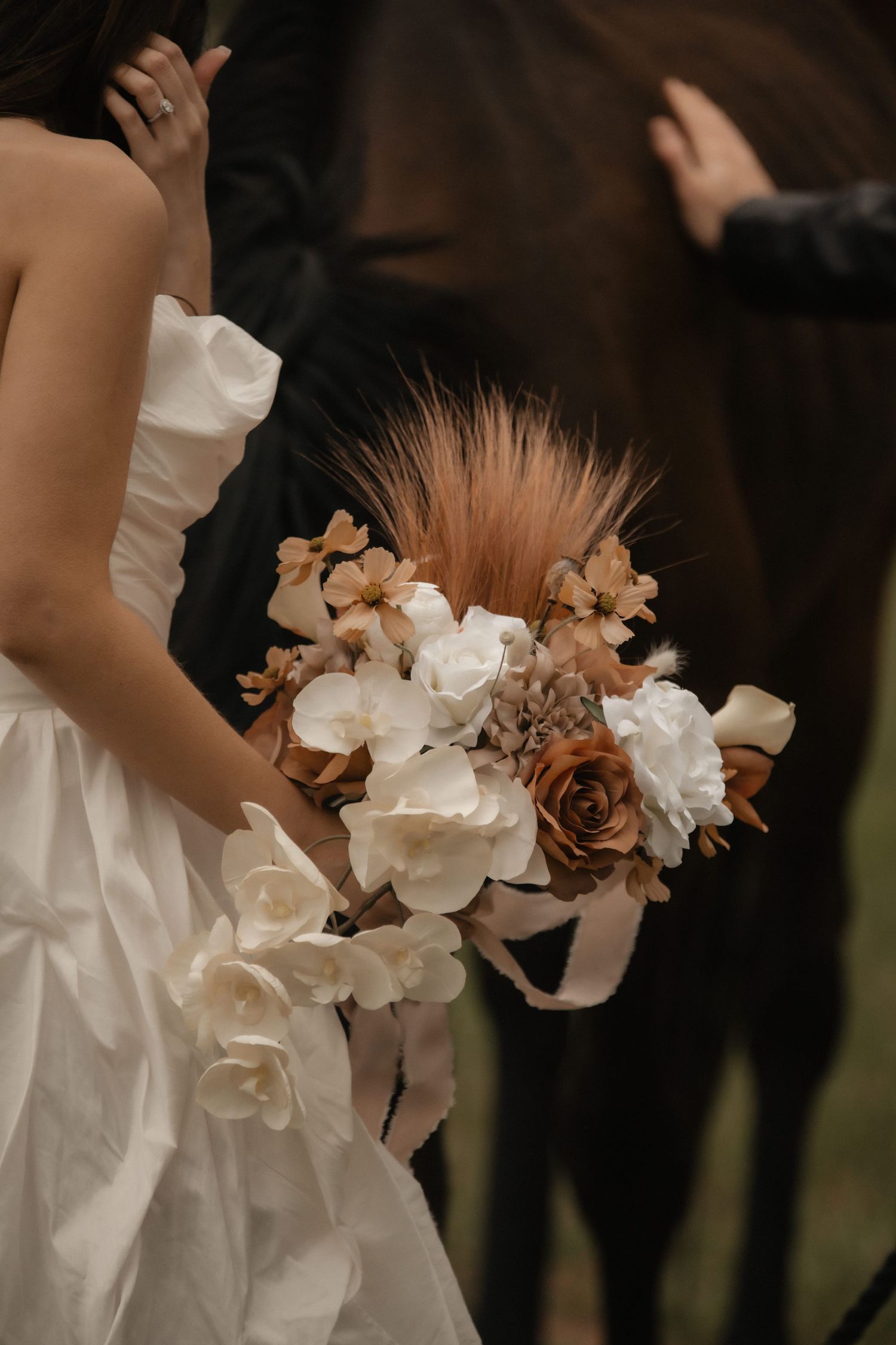 A wedding bouquet featuring white roses and brown accents held by someone in a white wedding dress.