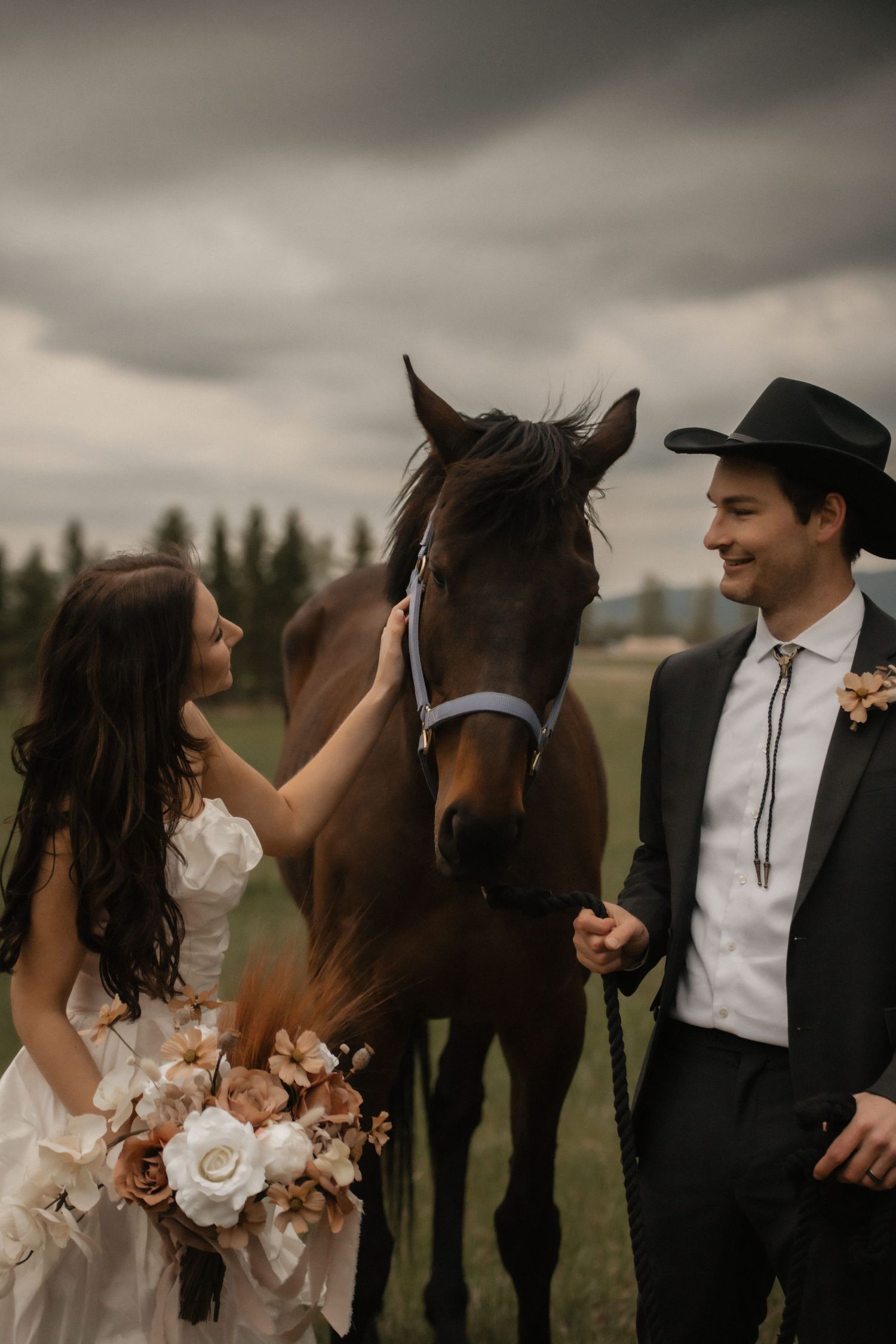 Romantic wedding couple poses with their elegant black horse in a rustic outdoor setting under moody gray skies.