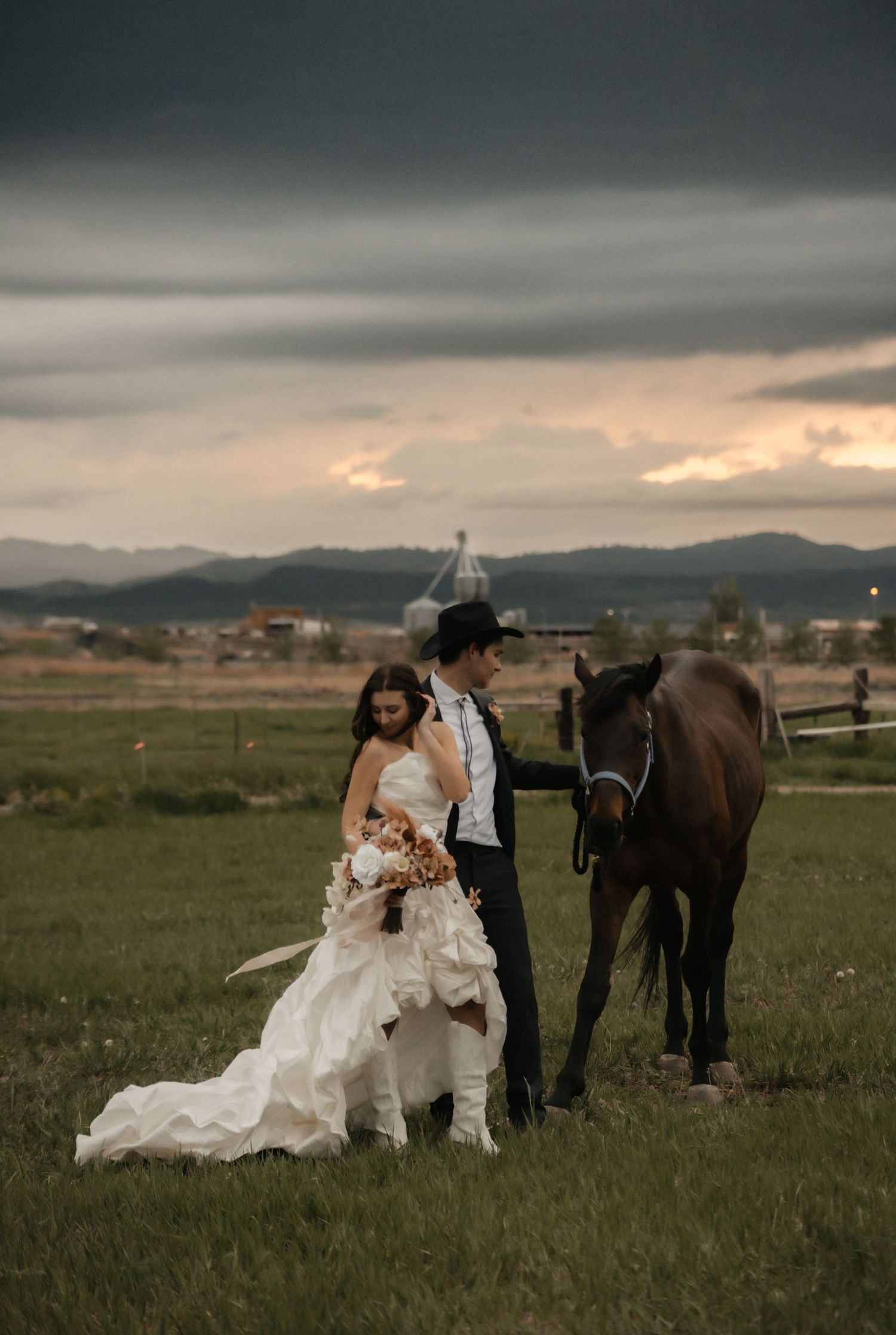A dramatic field wedding photoshoot with a horse under moody storm clouds at sunset.