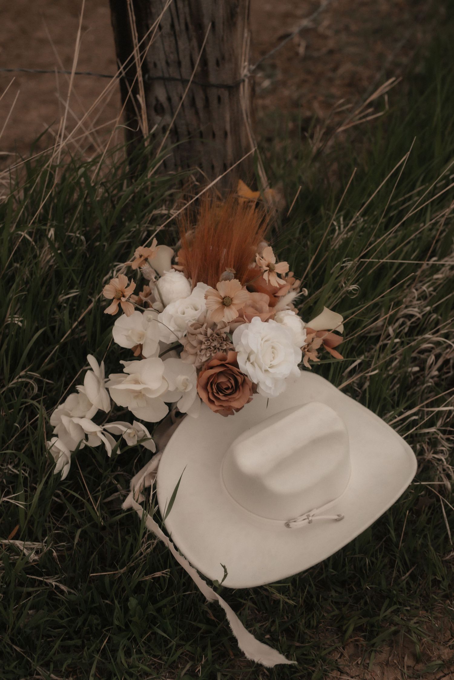 White cowboy hat decorated with delicate floral arrangements photographed against rustic background.