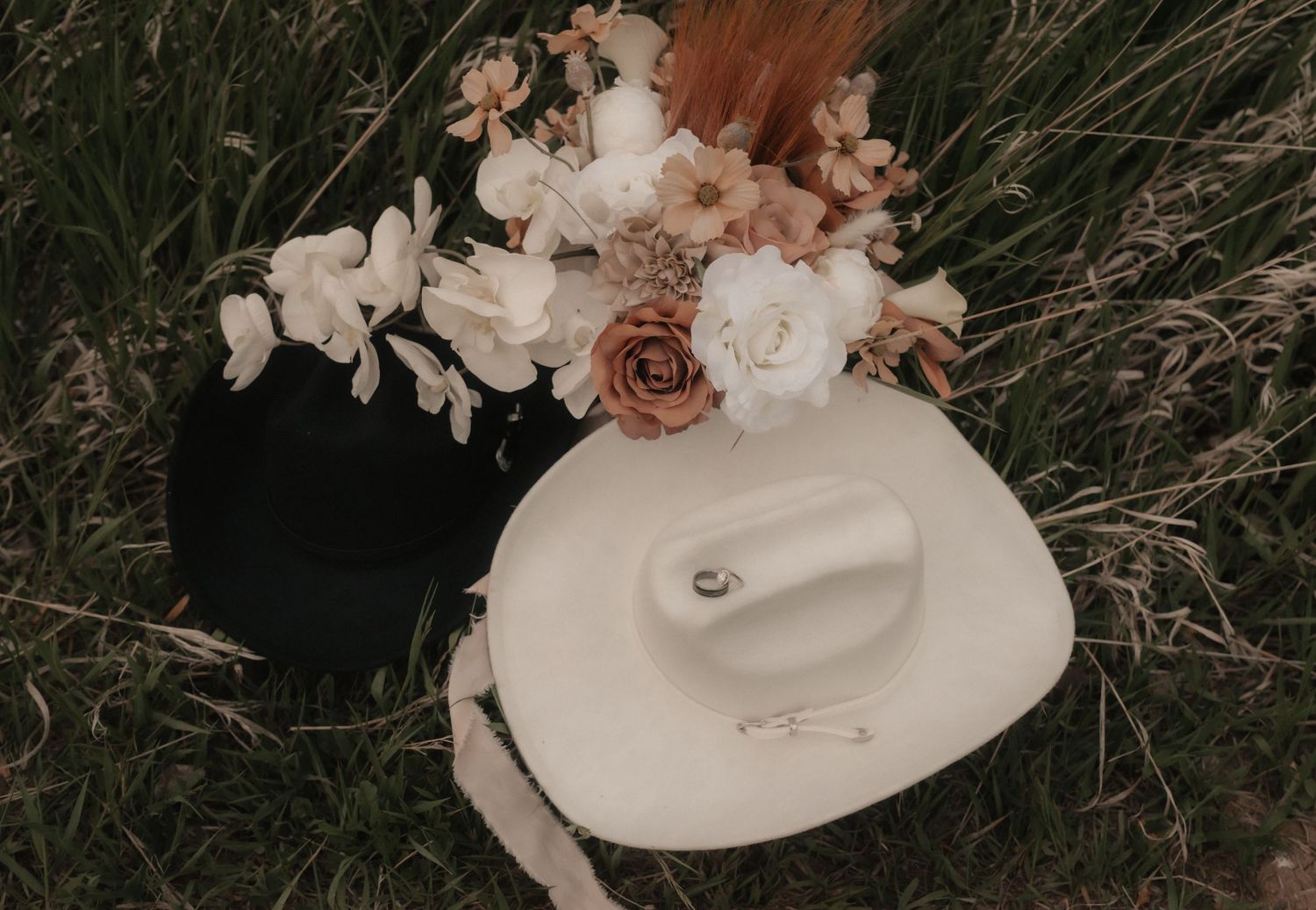 A rustic wedding bouquet featuring white and peach flowers lying in dried grass.