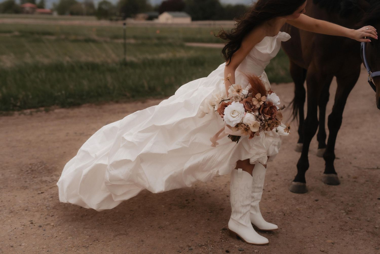 Wedding couple's boots and dress shown stepping on a dirt path in a rustic outdoor setting.