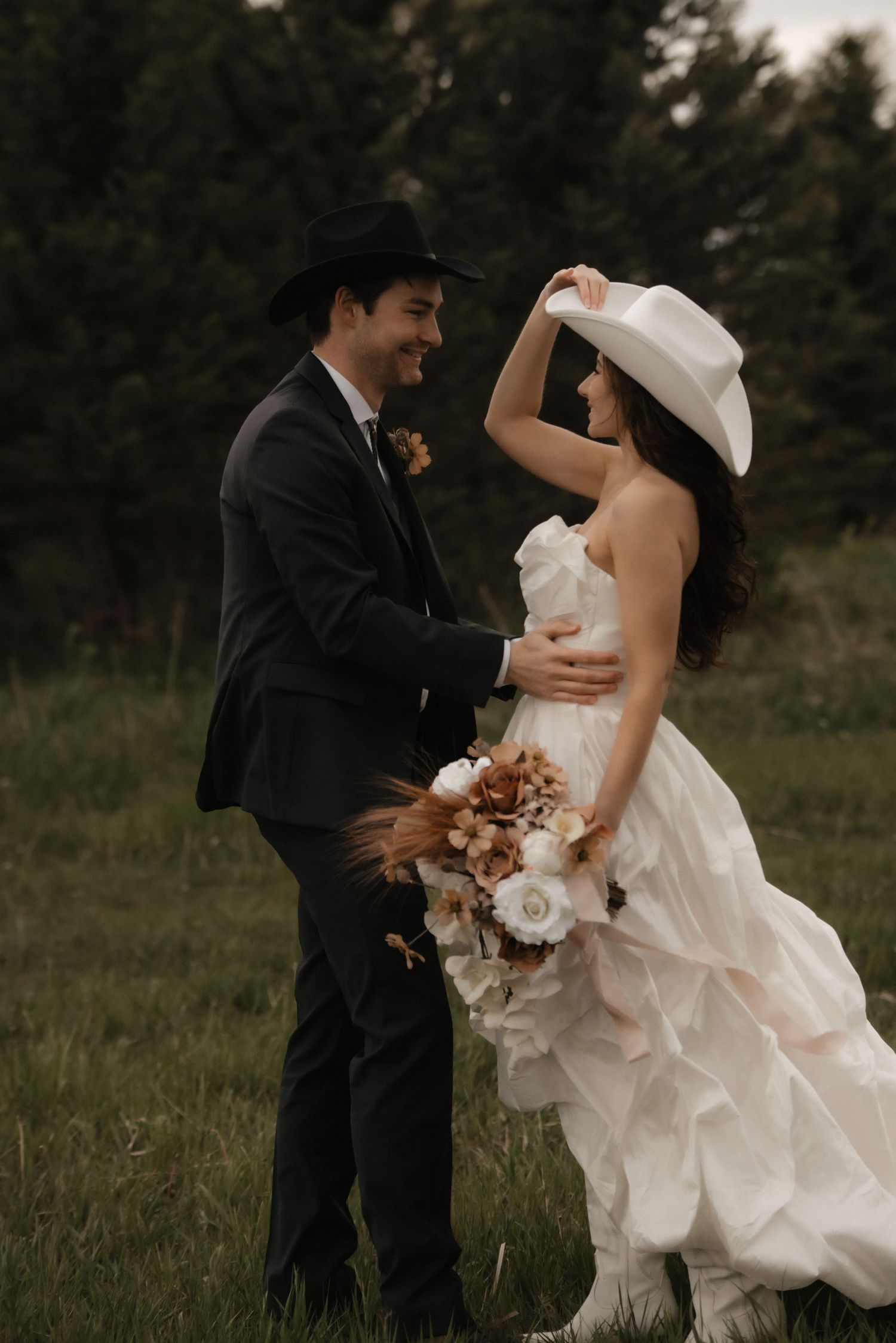 Couple dancing playfully in a grassy field during a wedding photoshoot with flowing white dress and black suit.