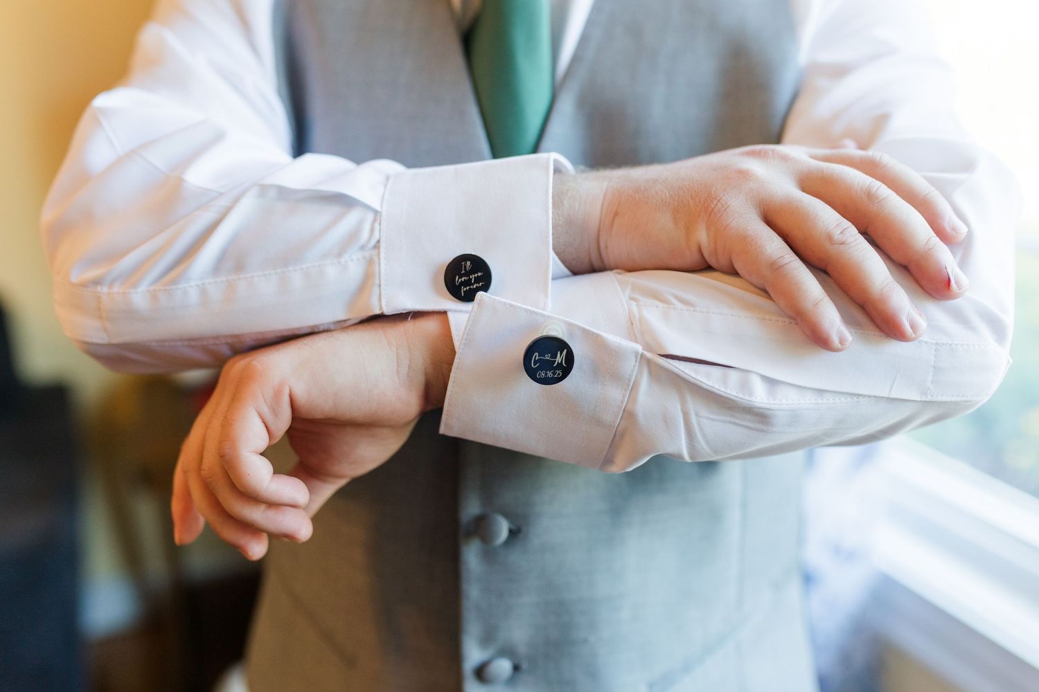 Close-up of hands adjusting silver cufflinks on a white dress shirt sleeve with mint green tie visible.