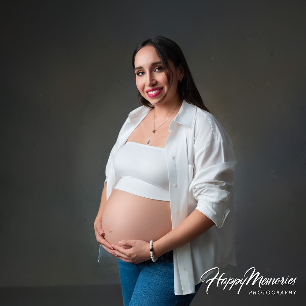 Smiling pregnant woman in white shirt and jeans cradling baby bump during maternity photo session.