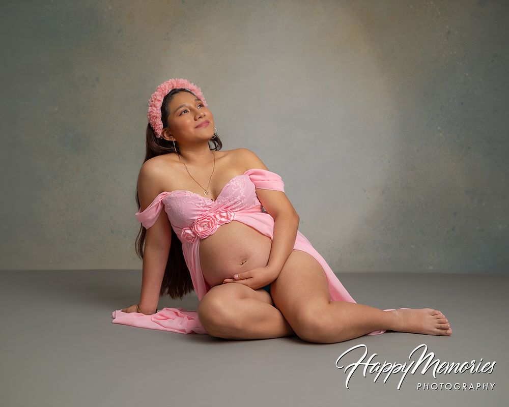 Pregnant woman in pink maternity outfit poses gracefully for a professional studio maternity photography session.