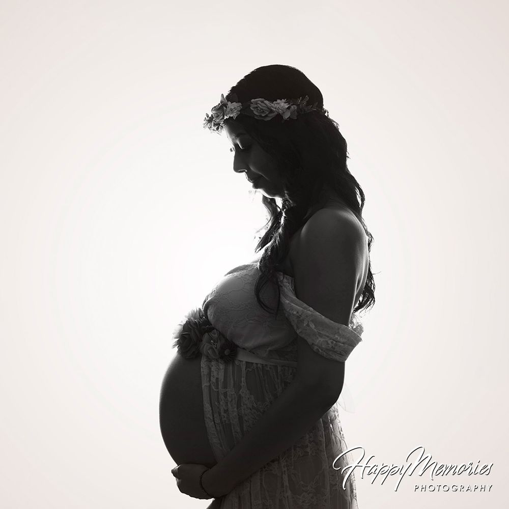 Stunning black and white silhouette of pregnant woman wearing flower crown cradling baby bump.